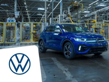 A blue SUV is positioned inside a brightly lit car manufacturing plant