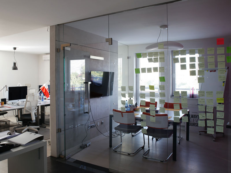 Modern office with a glass-walled meeting room on the right, featuring sticky notes on windows